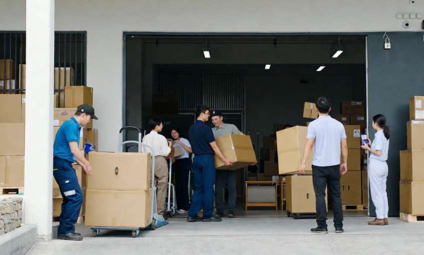 Költöztető csapat óvatosan rakod dobozokat egy teherautóba egy raktár előtt, professzionális és gyors munkavégzést bemutatva.